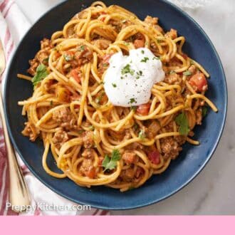 Pinterest graphic of a bowl of taco spaghetti with a dollop of sour cream and chopped cilantro.