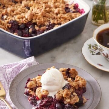 Berry crisp topped with ice cream with coffee and more crisp in the background.