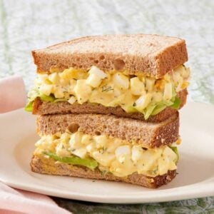 Egg salad sandwich with lettuce on a white plate.