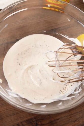 Creamy coleslaw dressing whisked together in a glass bowl.