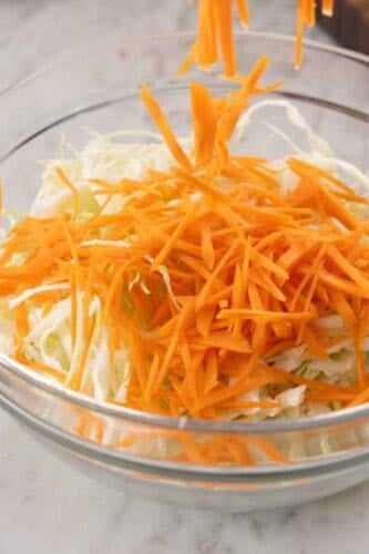 Shredded green cabbage and shredded carrots combined in a glass bowl.