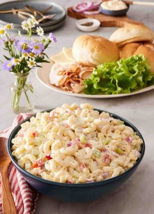 Macaroni pasta salad in a blue bowl with sandwich ingredients in the background.