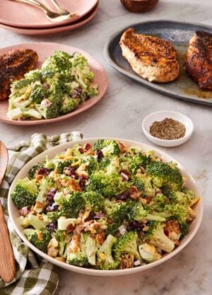 Broccoli salad in a bowl with more salad and cooked chicken breasts in the background.