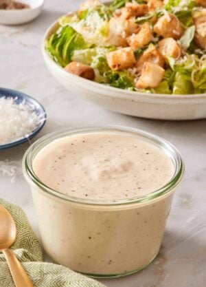 A small jar of Caesar dressing with a salad in the background.
