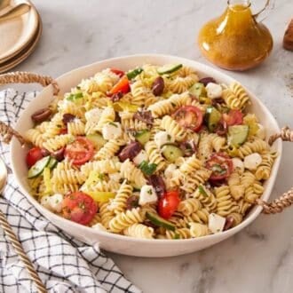 A ceramic dish of pasta salad with a serving spoon on a linen alongside.