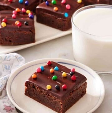 Cosmic brownie on a white plate next to a side of milk, with a platter of them in the background.