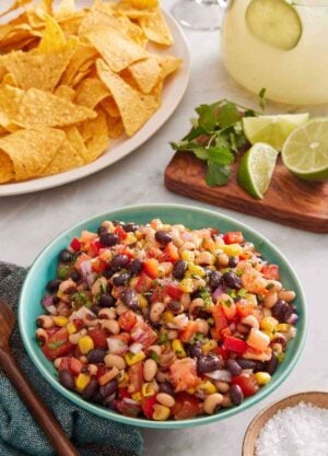 Cowboy caviar in a blue bowl with salt, chips, cilantro, and lime around it.