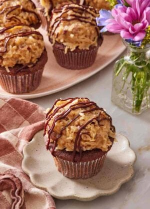 German chocolate cupcake on a small plate with a platter of cupcakes in the background.