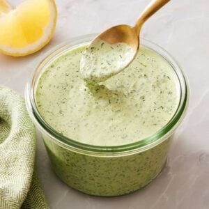 A spoon dipped into a jar of green goddess dressing, beside a green table linen.