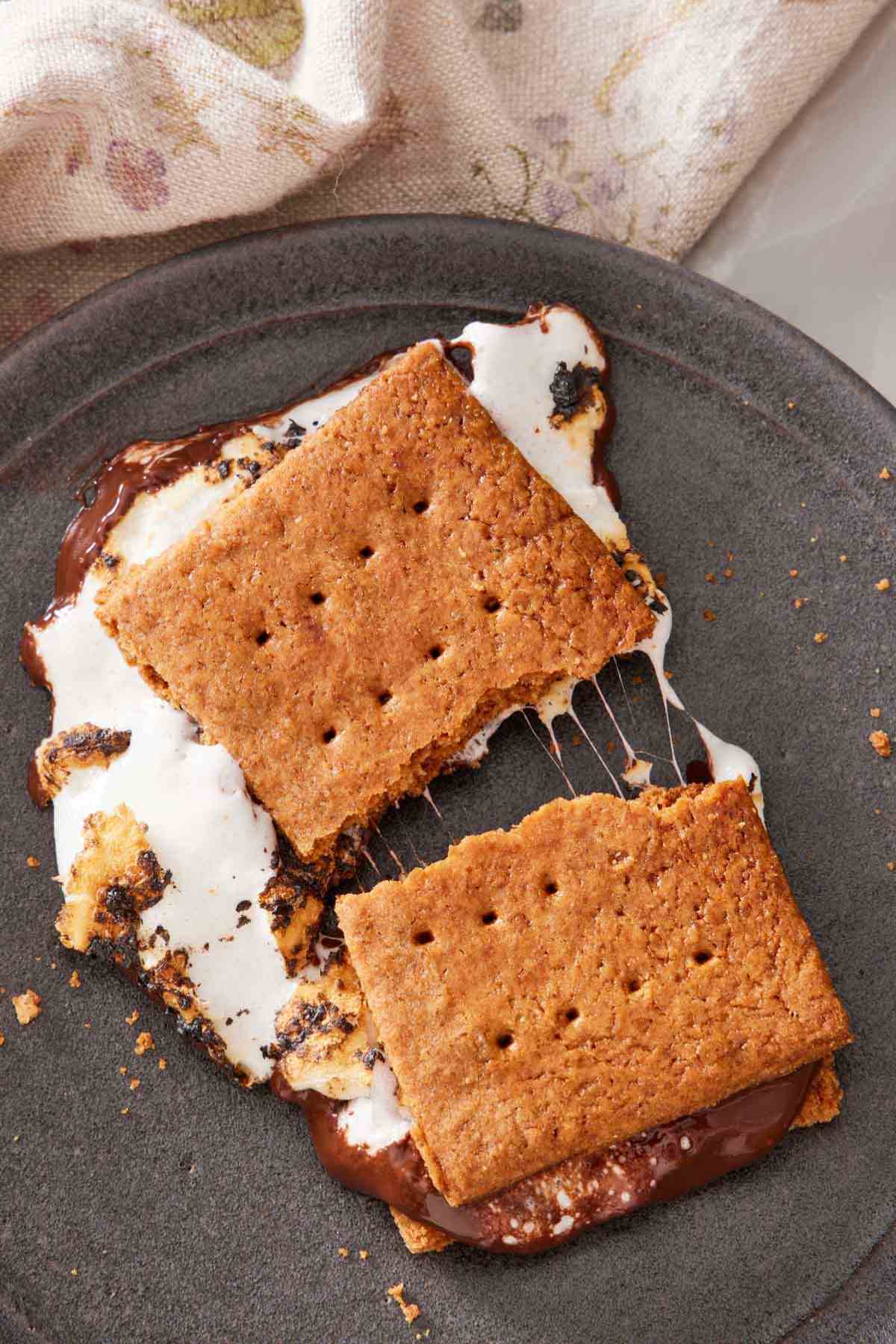 S'mores recipe split in two to show the gooey marshmallow on a gray plate.