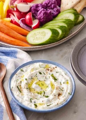 Tzatziki in a small blue bowl with a platter of vegetables half in frame.