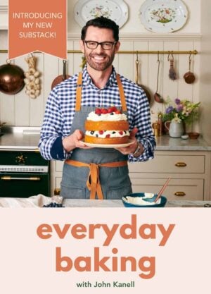 Image of John Kanell in his kitchen holding a cake on a cake plate to launch his new Substack.
