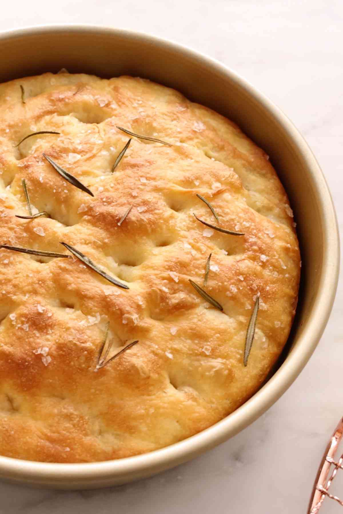 Focaccia baked in a round cake pan, sprinkled with flaky sea salt and rosemary.