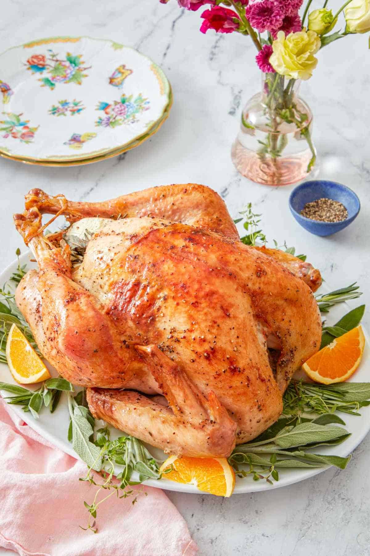 A roasted turkey on a bed of herbs and citrus on a platter.