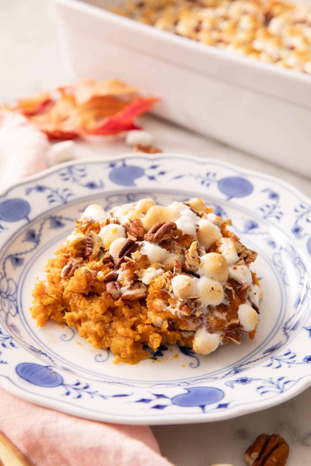 A serving of sweet potato casserole with marshmallows and pecans on a blue and white plate.