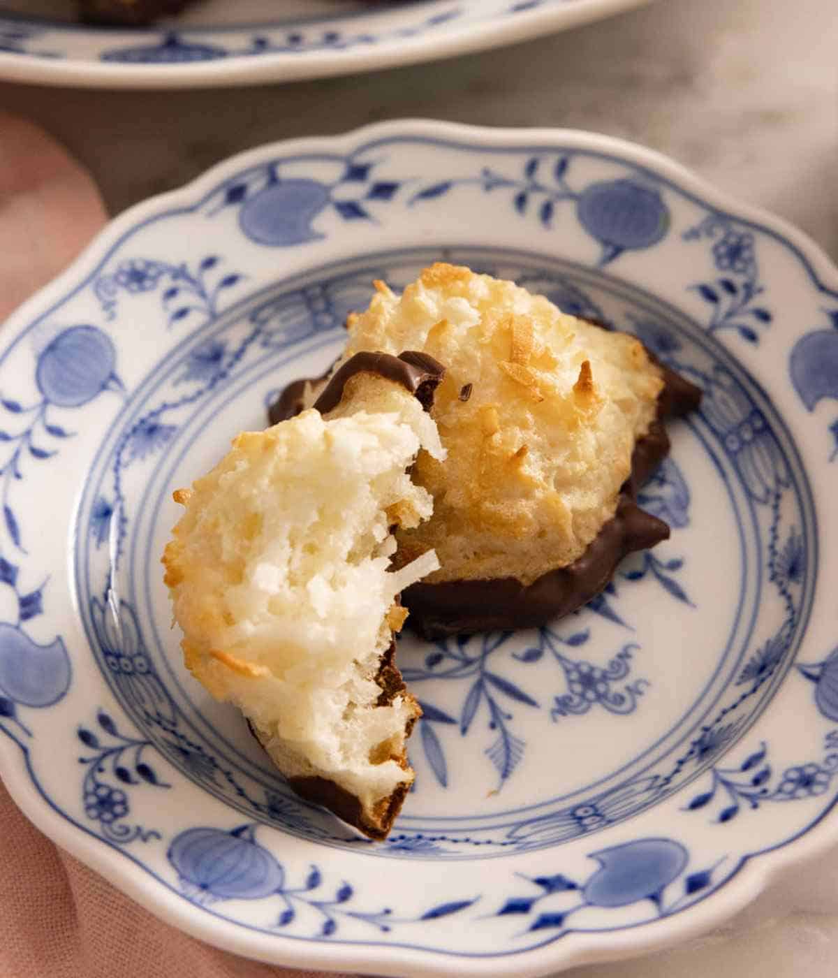 Two coconut macaroons, one with a bite taken out, on a patterned plate.