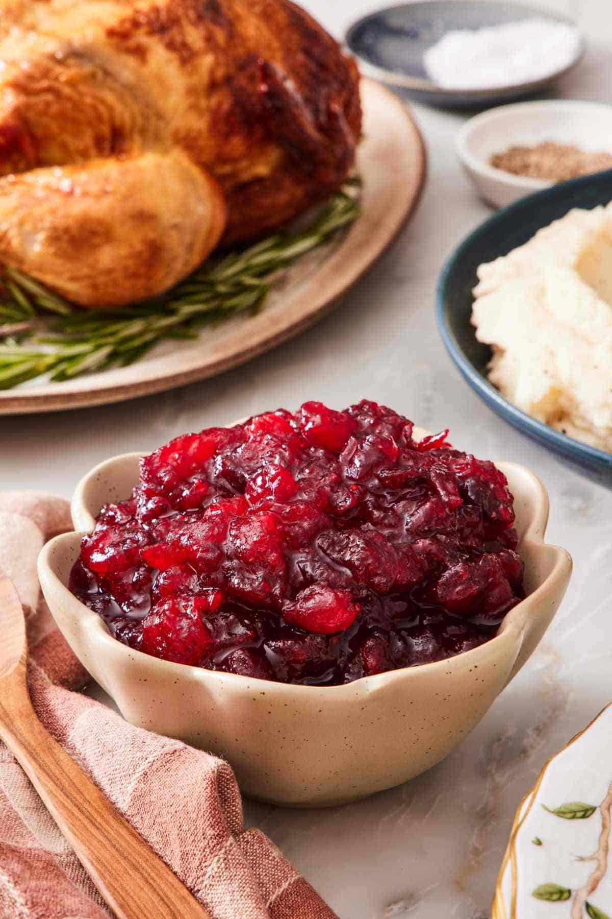 Close-up of a serving bowl of easy cranberry sauce with a turkey and mashed potatoes out of focus in the background.