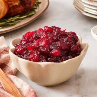 Cranberry sauce in a small serving bowl with plates and a roasted turkey in the background.