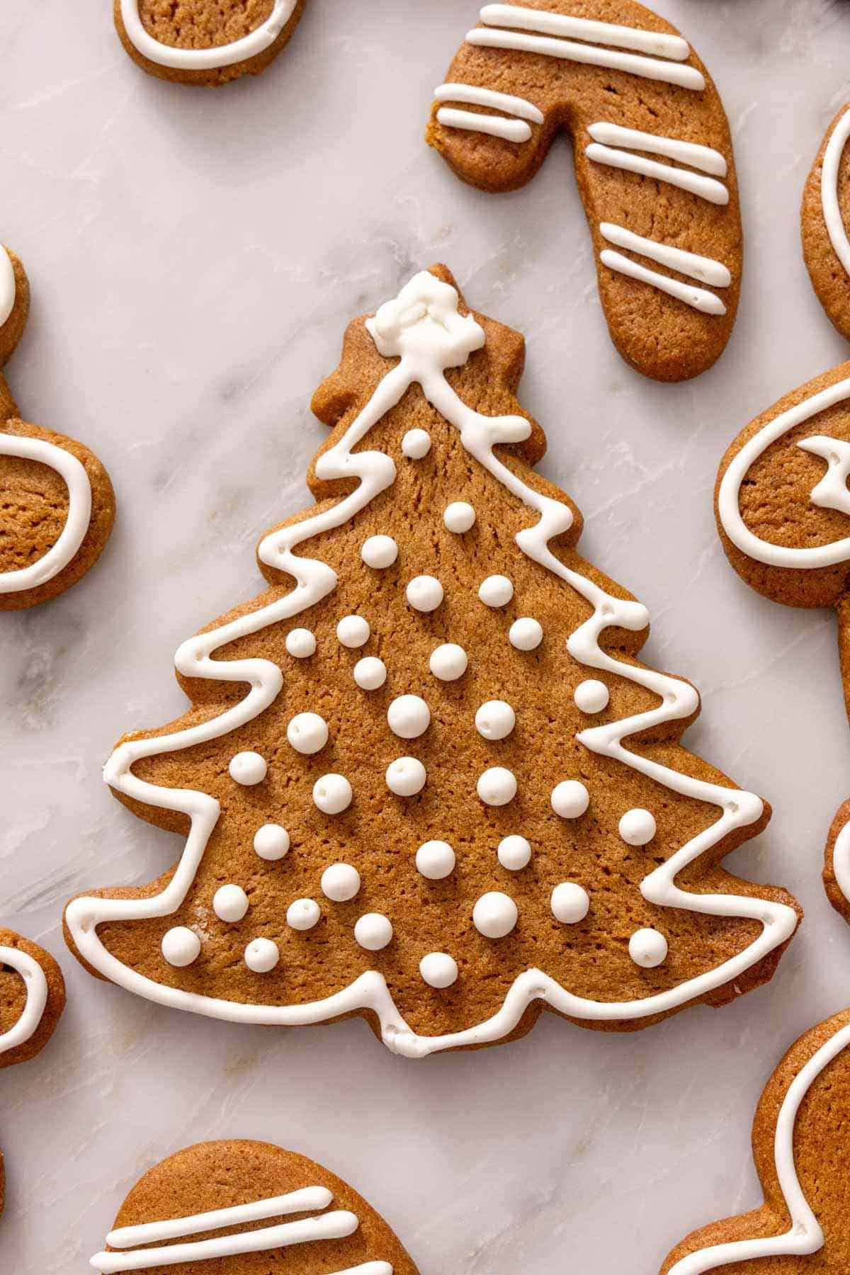 A gingerbread cookie shaped into a Christmas tree and decorated with white royal icing.