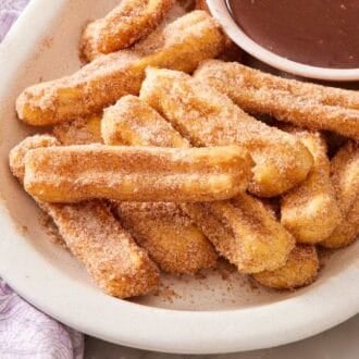 Air fryer churros on a white platter with a bowl of chocolate sauce mostly out of frame.
