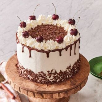 A black forest cake on a cake stand, with a cake server and small green serving plates on the side.