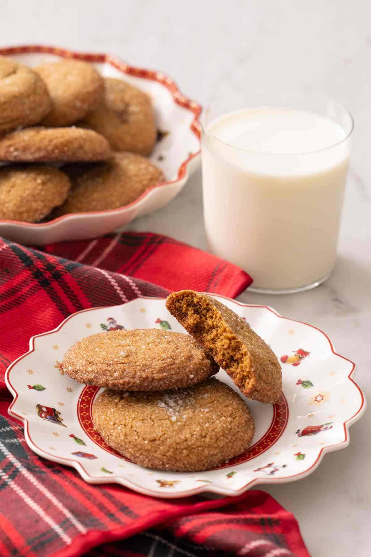 Gingersnap cookies on a Christmas-themed plate with a glass of milk in the background.