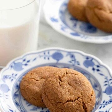 Gingersnaps on a patterned plate alongside a glass of milk.