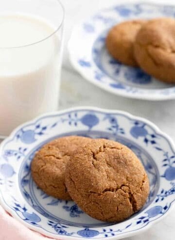 Gingersnaps on a patterned plate alongside a glass of milk.