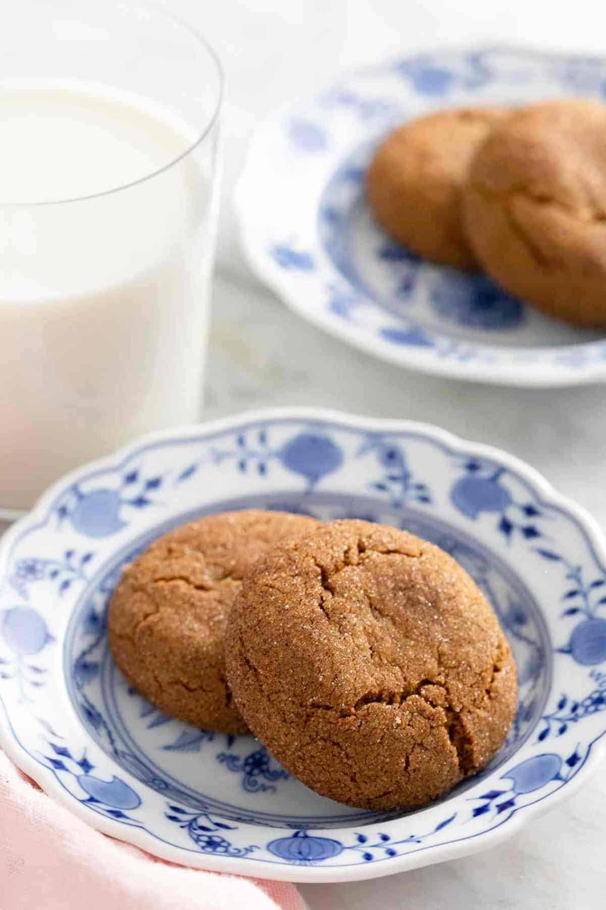 Gingersnaps on a patterned plate alongside a glass of milk.