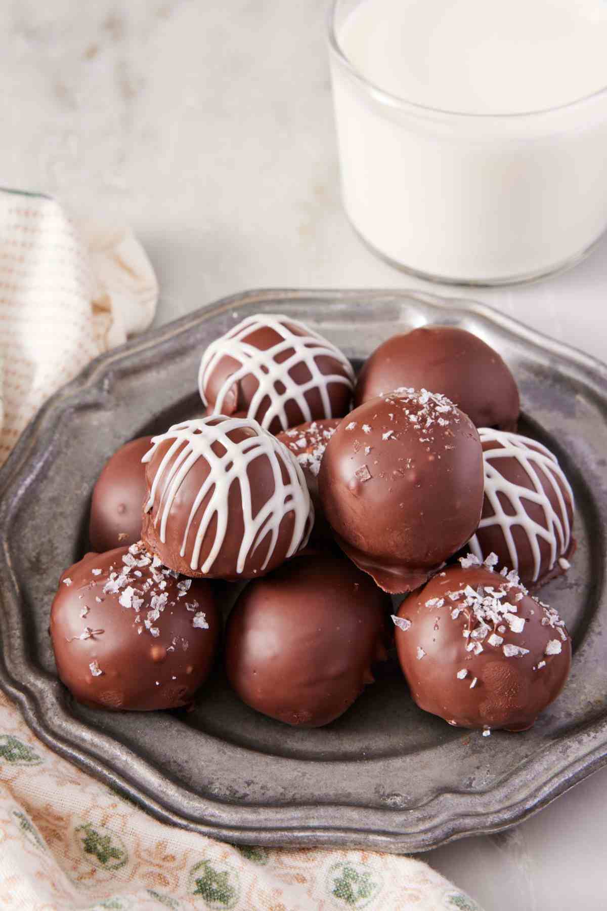 A pile of Oreo balls dipped in dark chocolate on a plate; some have a white chocolate drizzle and others sprinkled with sea salt.