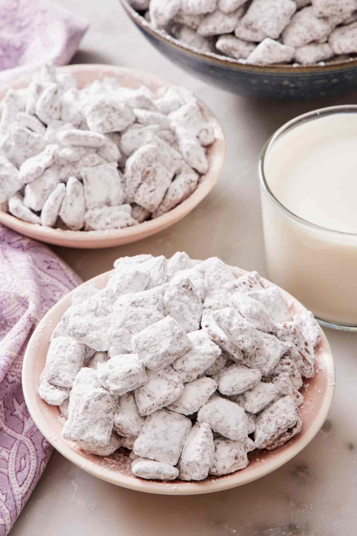 Bowls of homemade Muddy Buddies next to a glass of milk.