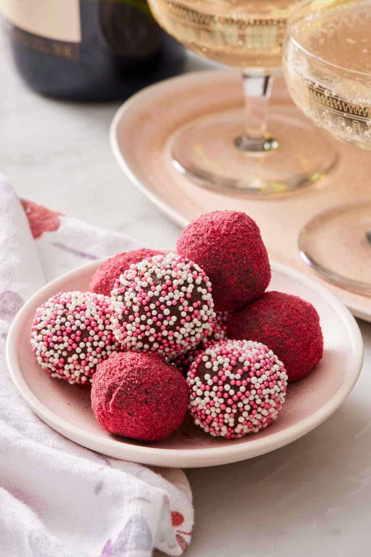Valentine's Day-themed chocolate truffles piled on a small plate. Some are coated with powdered freeze-dried berries, and the rest are coated with pink and white sprinkles.