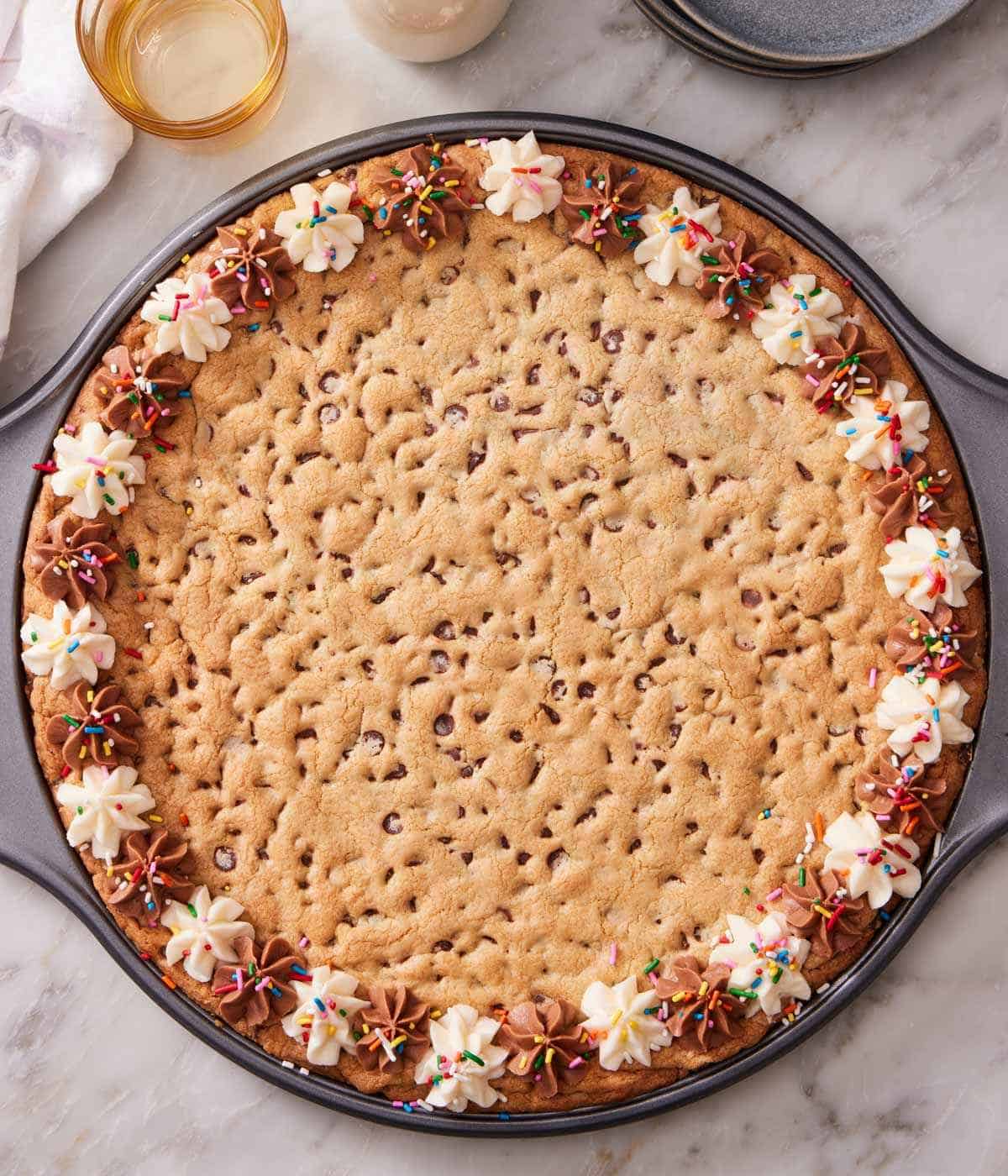 Overhead shot of a homemade cookie cake, the edges decorated with alternating types of frosting, and sprinkles.
