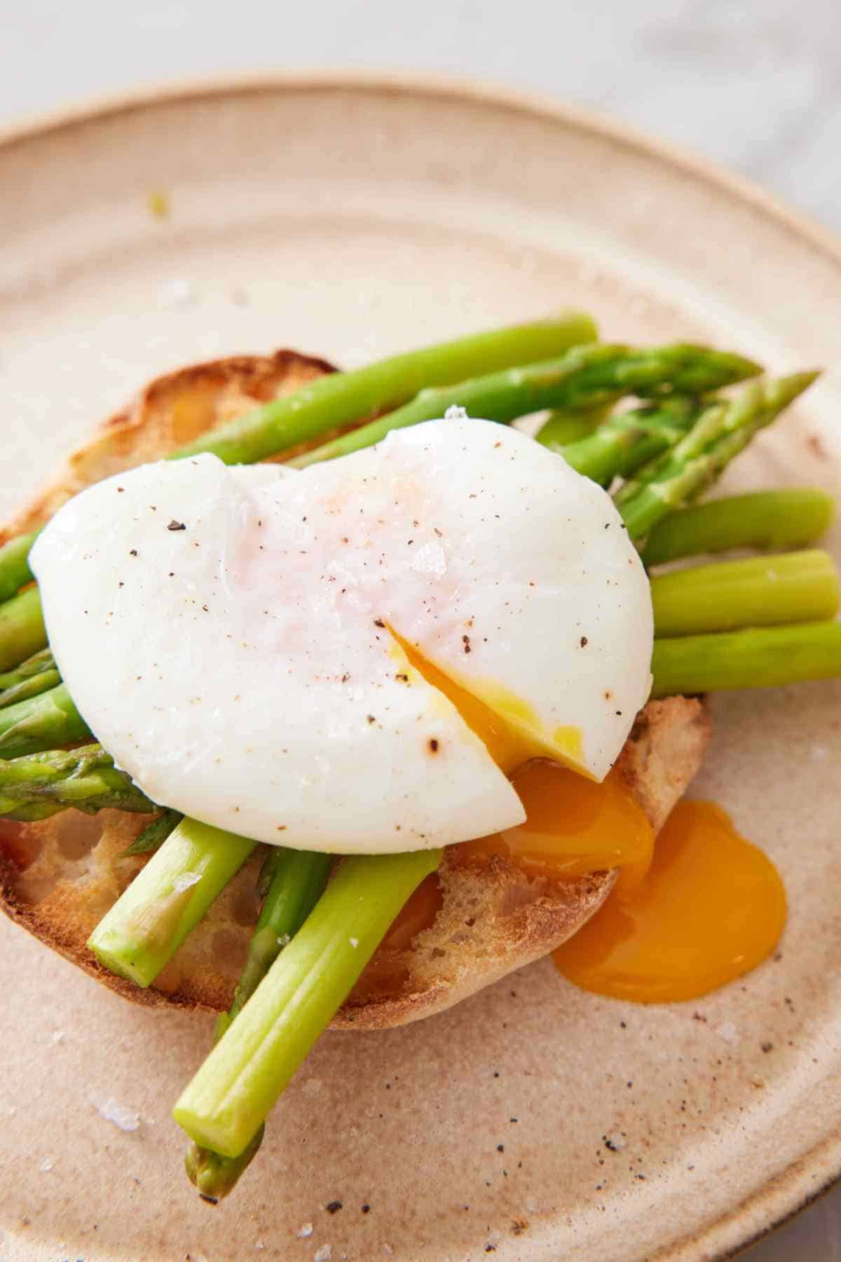 Close-up of a poached egg served over asparagus on an English muffin.
