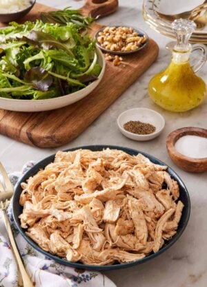 A bowl of Instant Pot shredded chicken with salad greens and dressing in the background.