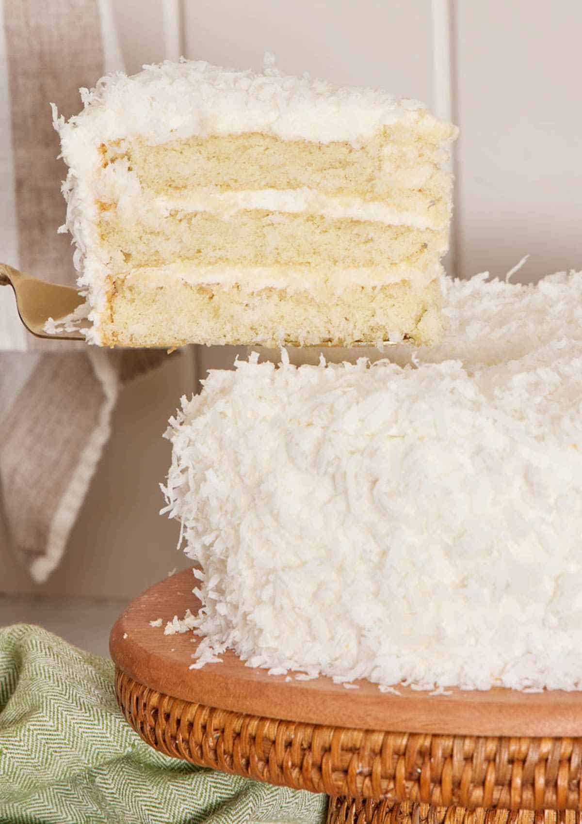 A slice of coconut cake lifted away from the rest of the cake with a cake server.