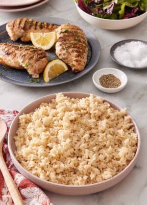 Serving bowl with Instant Pot brown rice, with grilled chicken breasts and salad greens in the background.