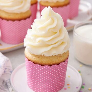 A frosted moist vanilla cupcake on a small plate.