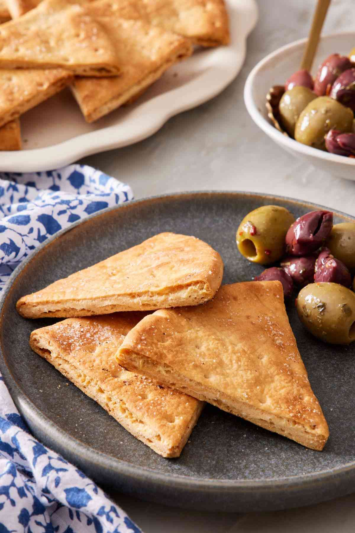 Homemade pita chips on a plate with marinated olives.