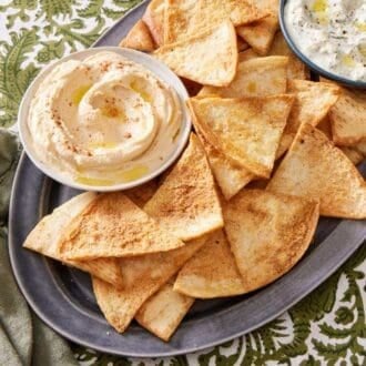 A platter of homemade pita bread recipe with small bowls of tzatziki and hummus on the platter as well.