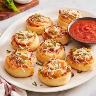 A platter of pizza rolls with a small bowl of pizza sauce.