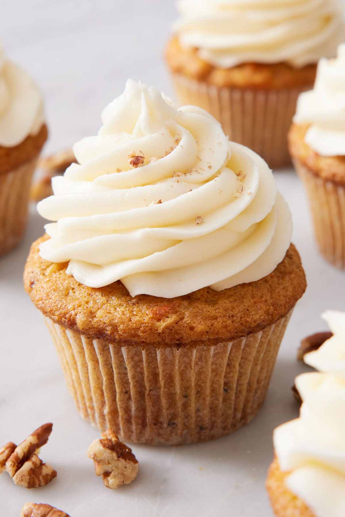 Close-up of a carrot cake cupcake with more cupcakes out of focus surrounding it.