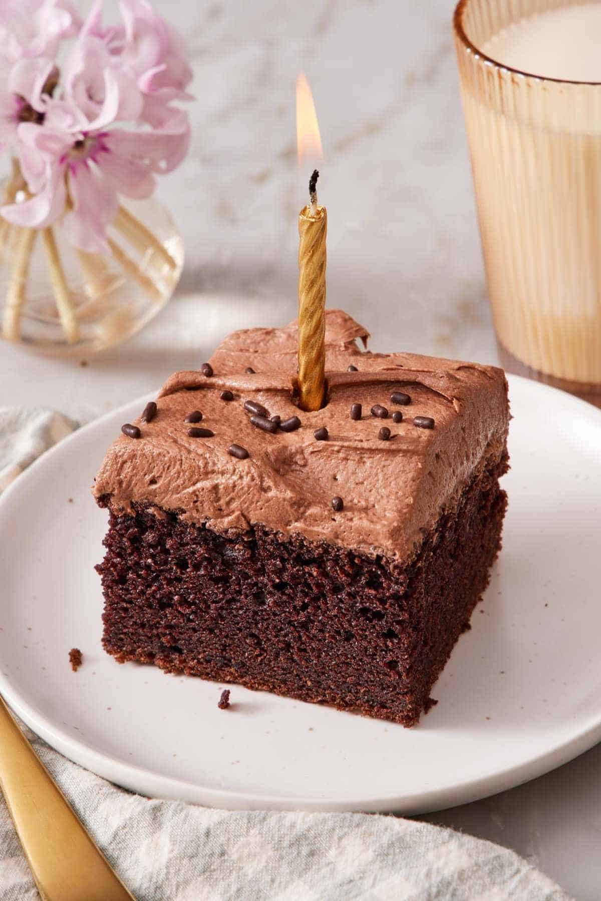 A slice of chocolate sheet cake with a lit candle in it.