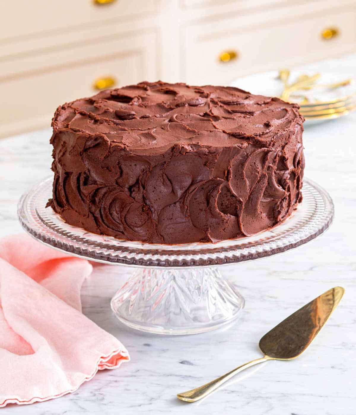 A devil's food cake on a cake stand with a cake server on the counter beside it.