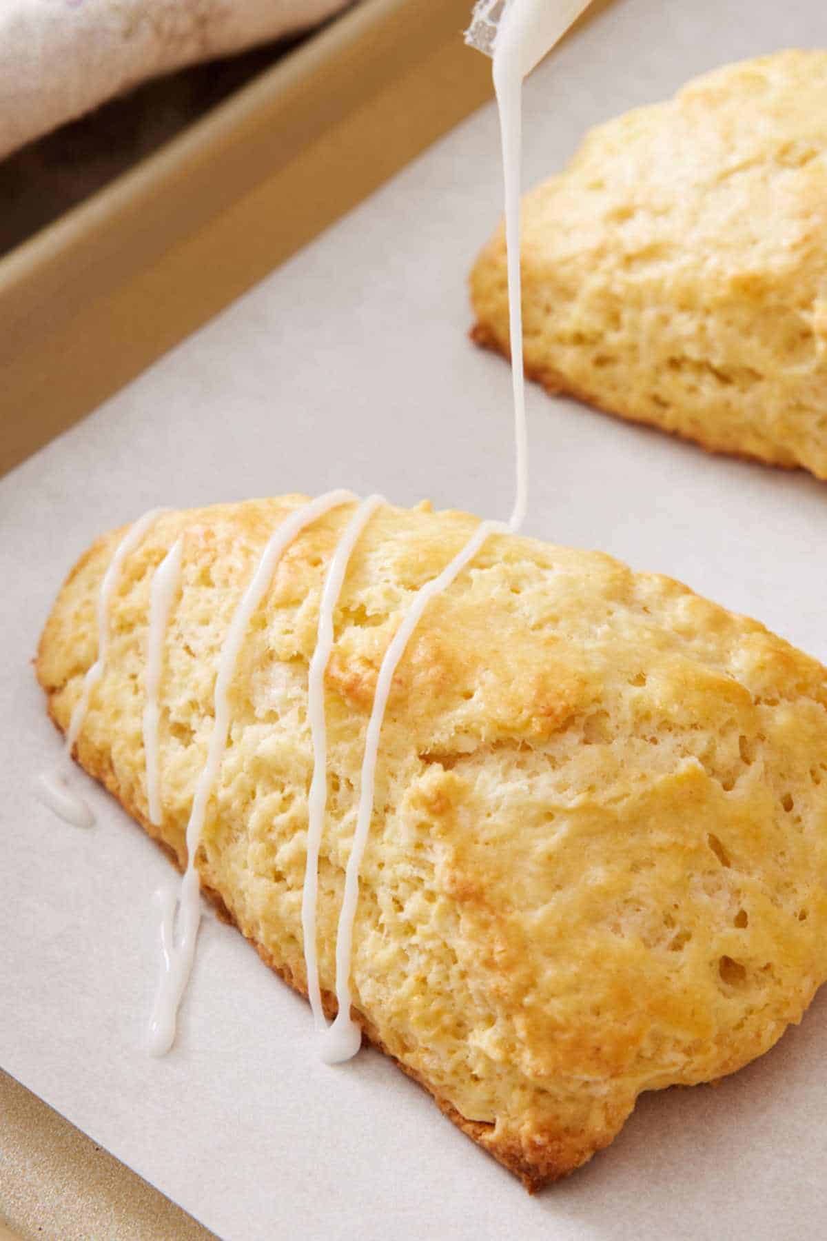Close-up of a lemon scone with lemon glaze drizzled over the top from a piping bag.
