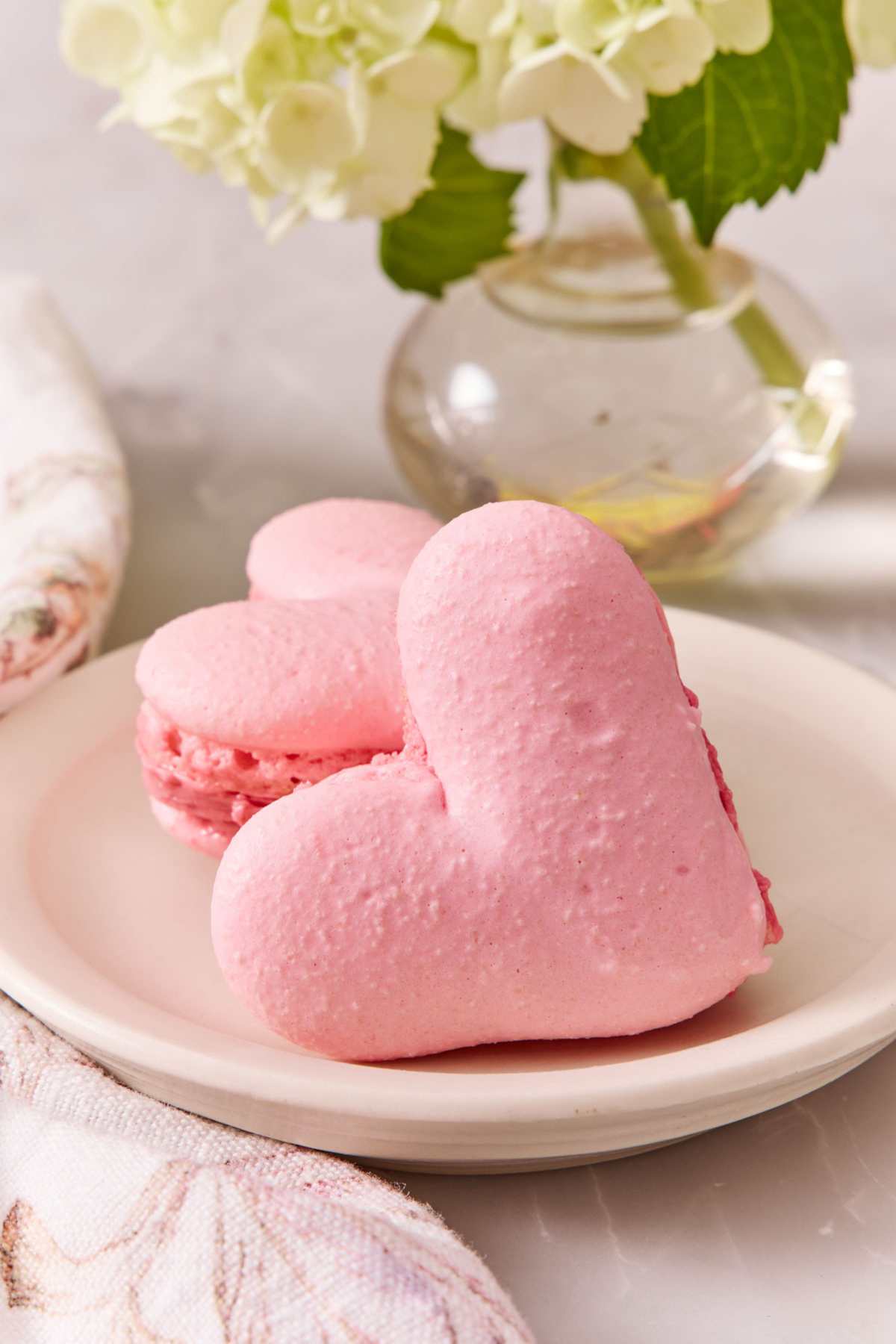 Two heart-shaped macarons on a plate, one leaning against the other.