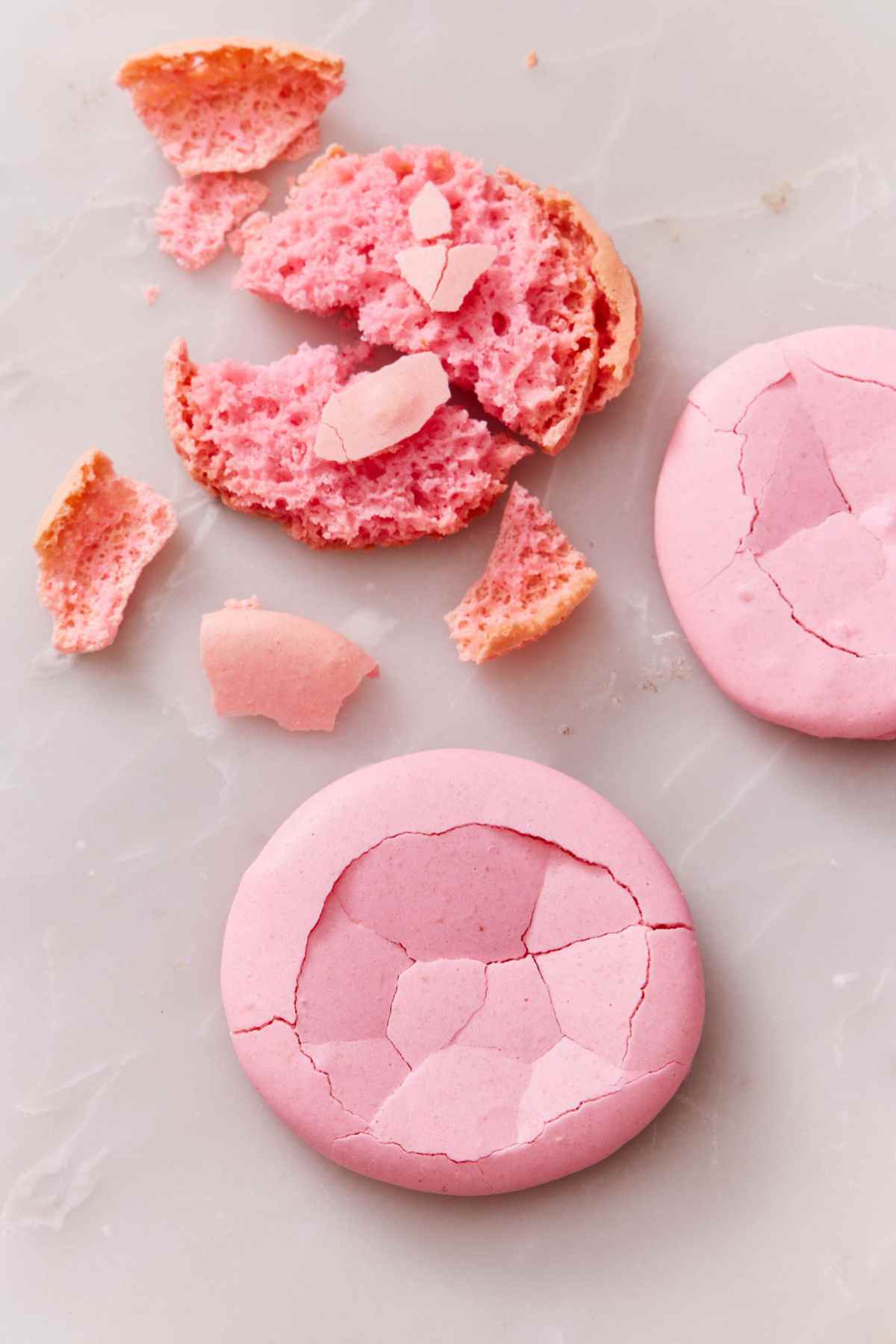 Macarons with a hollow shell, cracked to show the hollowness. Pieces of one macaron alongside to show the interior.