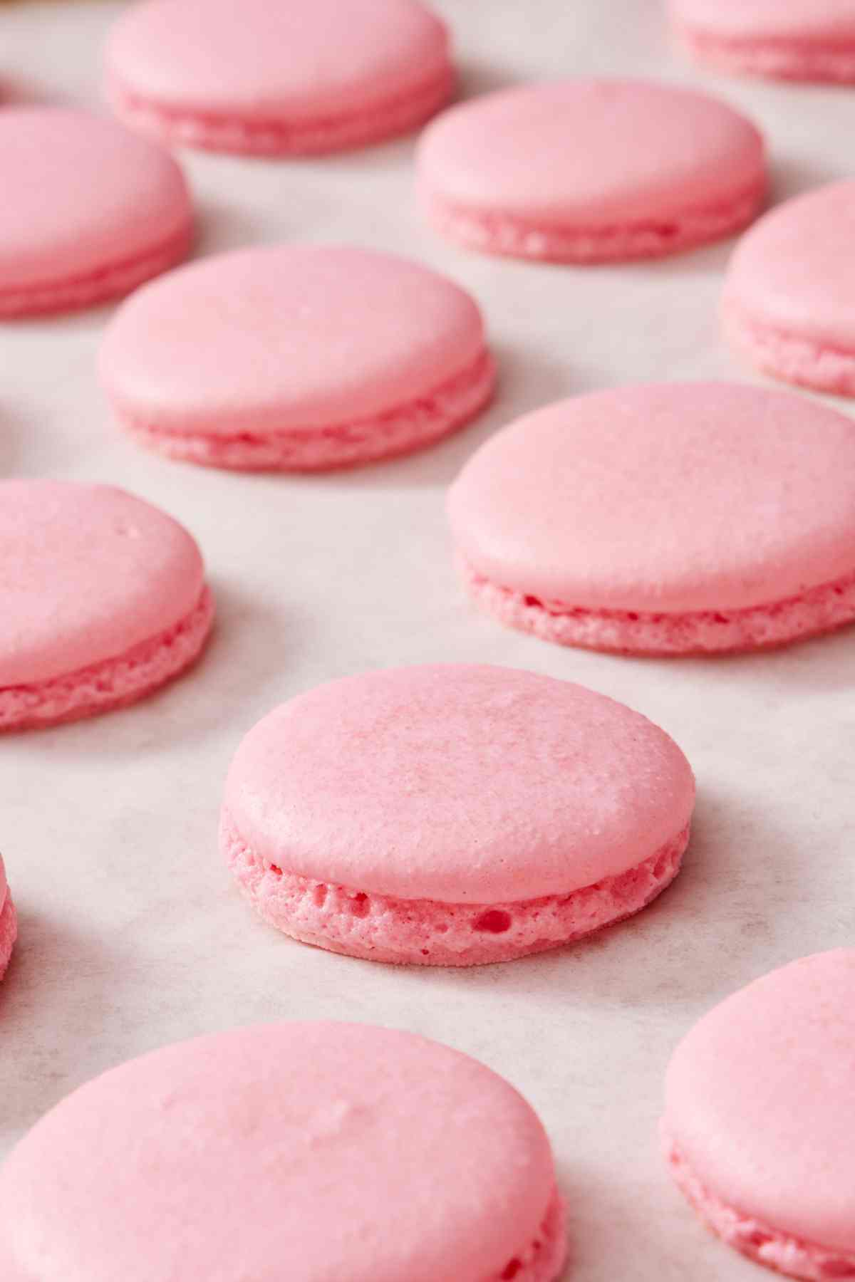 Several properly baked macarons with feet on a countertop.