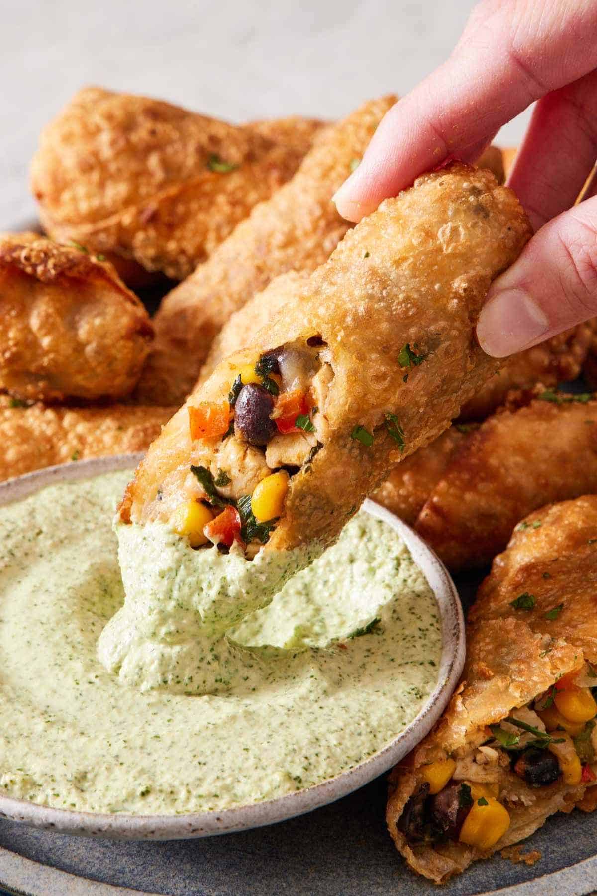 Half a southwest egg roll dipped into a sauce. More egg rolls on a platter around it.
