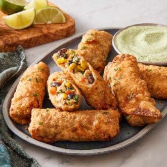 A platter of southwest egg rolls with homemade dipping sauce. A blue table linen on the side.